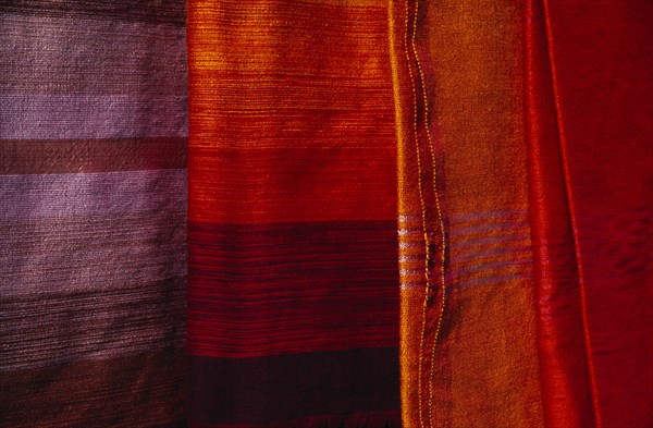MOROCCO, Essaouira, Detail of red  orange and pale purple / blue woven textiles.