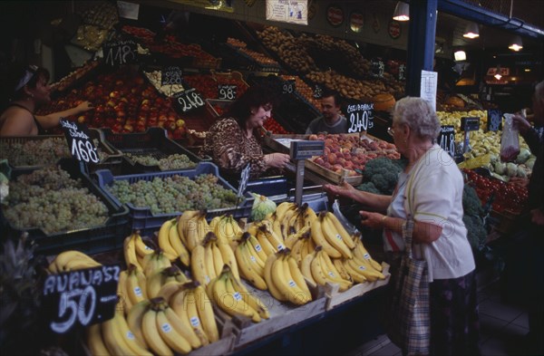 HUNGARY, Budapest, Fruit and vegetable stall in Central Market with woman customer and vendor making cash transaction. Eastern Europe