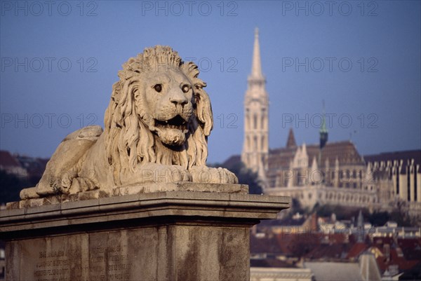 HUNGARY, Budapest, Stone statue of lion on Chain Bridge with Matyas Church in distance behind. Eastern Europe