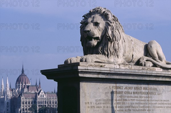 HUNGARY, Budapest, Stone statue of lion on Chain Bridge with Parliament building in distance behind. Eastern Europe