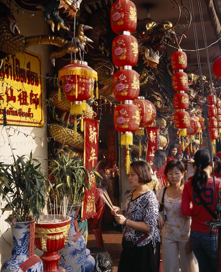 THAILAND, Bangkok, China Town, Wat Traimit.  People offering prayers and incense at temple decorated with red Chinese lanterns and strings of coloured lights for Chinese New Year.