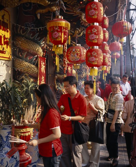 THAILAND, Bangkok, China Town, Wat Traimit.  People offering prayers and incense at temple decorated with red Chinese lanterns and strings of coloured lights for Chinese New Year.