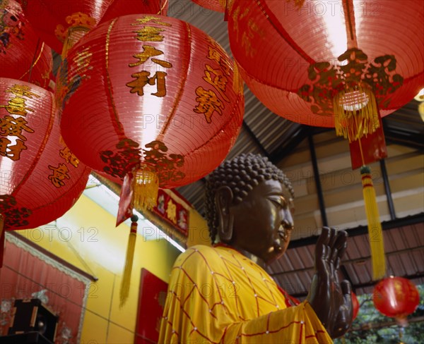 THAILAND, Bangkok, Sathorn District, Charoen Krung.  Buddha statue bathed and dressed in auspicious gold and red silk for Chinese New Year with red New Year lanterns in the foreground.