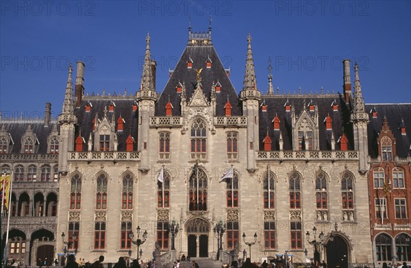BELGIUM, West Flanders, Bruges, The Markt (Market Place). Exterior facade of old town building with red painted window frames  roof vents and gables with spires and gold statue of the archangel Michael slaying the devil.