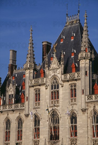 BELGIUM, West Flanders, Bruges, The Markt (Market Place). Exterior facade of old town building with red painted window frames  roof vents and gables with spires and gold statue of the archangel Michael slaying the devil.