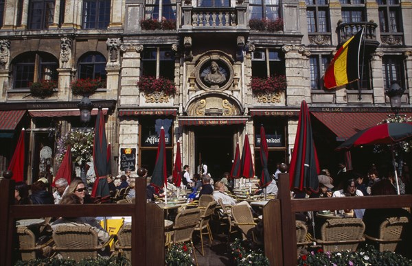 BELGIUM, Brabant, Brussels, Grand Place.  Busy cafe with people sitting at outside tables in the sunshine.  Part view of building facade with stone balcony and flower filled window boxes. UNESCO World Heritage Site