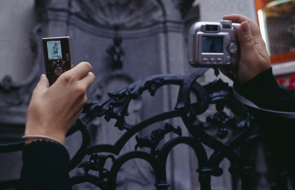 BELGIUM, Brabant, Brussels, Cropped view of visitors to the Manneken-Pis statue holding up digital camera and mobile phone to take photograph.