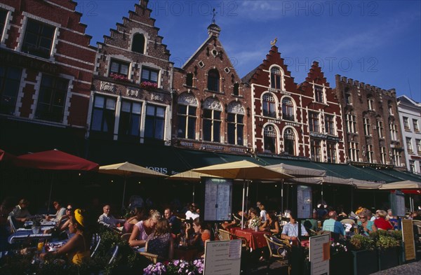 BELGIUM, West Flanders, Bruges, The Markt (Market Place)  Line of cafes with busy outside tables under green awnings and red umbrellas with menus displayed at side.