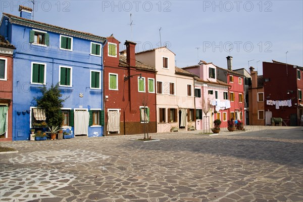 ITALY, Veneto, Venice, Colourful houses in a square on Burano. One of the few inhabited islands in the lagoon. Laundry hanging to dry outside windows.