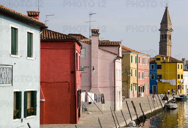 ITALY, Veneto, Venice, Colourful houses beside a canal on Burano. One of the few inhabited islands in the lagoon. The leaning tower of San Martino church in the distance