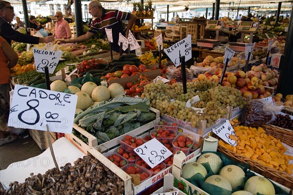ITALY, Veneto, Venice, The vegetable market with vendor and shoppers beside the produce in the San Polo and Santa Croce district beside the Rialto Bridge on the Grand Canal