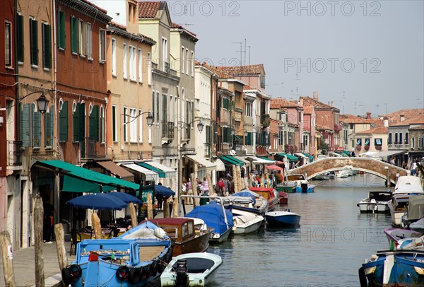 ITALY, Veneto, Venice, The main canal beside Fondamente dei Vetrai on Murano Island with boats moored at the quayside and a bridge across the canal