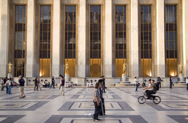 FRANCE, Ile de France, Paris, Tourists beneath the gilded statues and the facade of the Theatre National de Chaillot in the central square of the Palais de Chaillot at sunset