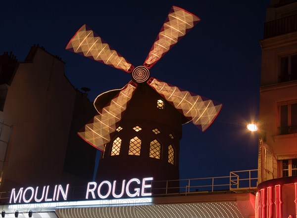 FRANCE, Ile de France, Paris, Montmartre The Moulin Rouge nightclub illuminated at night with the windmill sails rotating