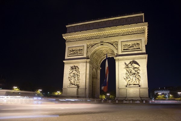FRANCE, Ile de France, Paris, Streaked lights of traffic passing the Arc de Triomphe illuminated at night