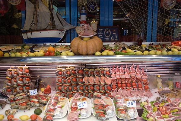 FRANCE, Ile de France, Paris, Greek restaurant window display in the Latin Quarter showing seafood and meat kebabs with a pigs head on a plate
