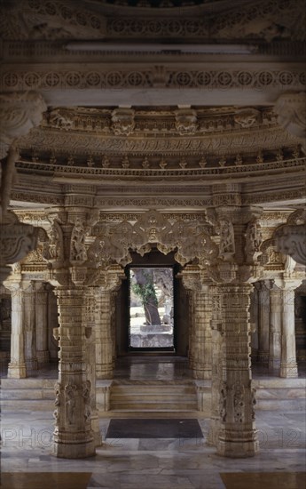 INDIA, Rajasthan, Mount Abu, Dilwara Temple complex dating from 11th-13th century A.D.  Detail of intricately carved white marble ceiling and supporting pillars framing view to outside courtyard.