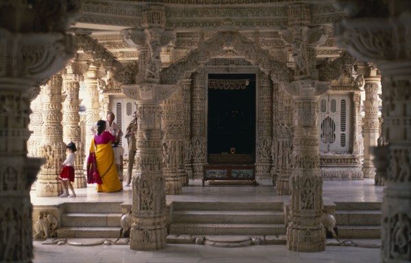 INDIA, Rajasthan, Mount Abu, Dilwara Temples.  Vimal Vasahi 1031 A.D. Visitors on raised platform below intricately carved white marble ceiling and supporting pillars .