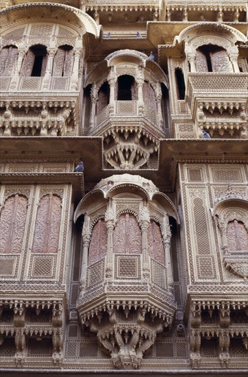 INDIA, Rajasthan, Jaisalmer, Detail of intricately carved facade of sandstone merchant’s house or Haveli with pigeons roosting on the overhanging ledges.