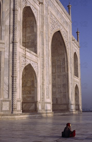 INDIA, Uttar Pradesh, Agra, Taj Mahal.  Part view of white marble exterior with woman sitting on polished floor in foreground.