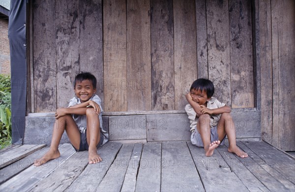 INDONESIA, Sumatra, Children, Two laughing children sitting on wooden floor of building.