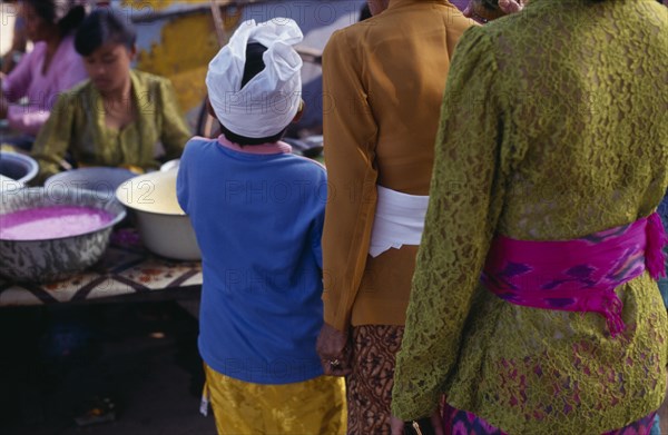 INDONESIA, Bali, Traditional Dress, Cropped view from behind of young boy in traditional dress standing beside two smartly dressed women.
