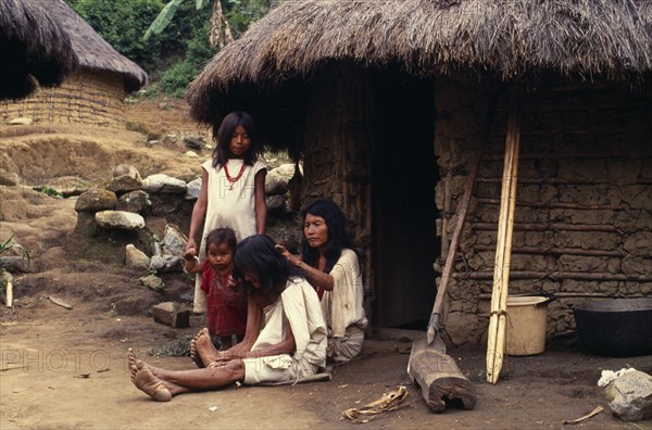 COLOMBIA, Sierra Nevada de Santa Marta, Kogi-Wiwa family outside mud-wattle/grass thatched home in Avingue village on South side of Sierra Nevada de Santa Marta. Mother de-lousing grandmother's hair. Strings of red glass beads a sign of family wealth.   Tribal Indigenous Colombian Columbia Hispanic Indegent Latin America Latino Mum South America