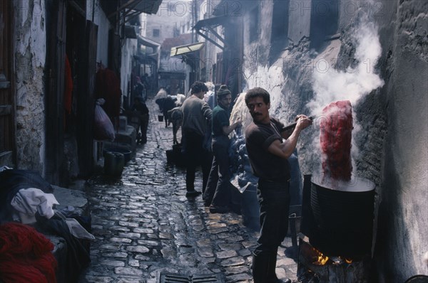 MOROCCO, Fez, Street in the wool dyeing souk with man in foreground lifting skein of yarn from vat of dye.