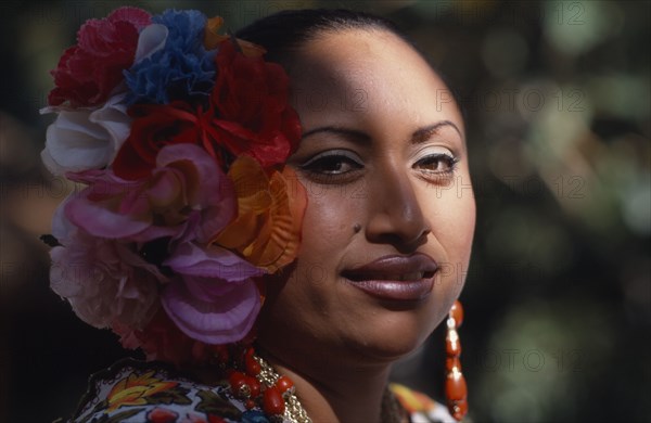 MEXICO, Yucatan, Chichen Itza, Head and shoulders portrait of female singer and dancer wearing silk flowers in her hair.