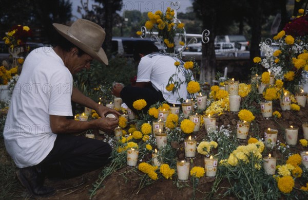 MEXICO, Michoacan, Purepecha, Tarascan Indian lighting candles on grave decorated with marigold flowers for Night of the Dead in Tzintzuntzan Cemetery.