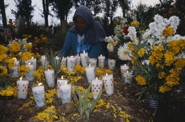 MEXICO, Michoacan, Purepecha, Tarascan Indian woman lighting candles on grave decorated with marigold flowers for Night of the Dead in Tzintzuntzan Cemetery.