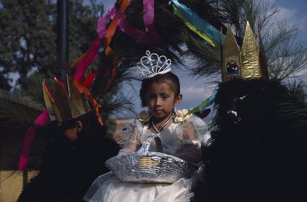 MEXICO, Tlaxcala, Little girl dressed in white flanked by two masked attendants in costume on float during carnival.