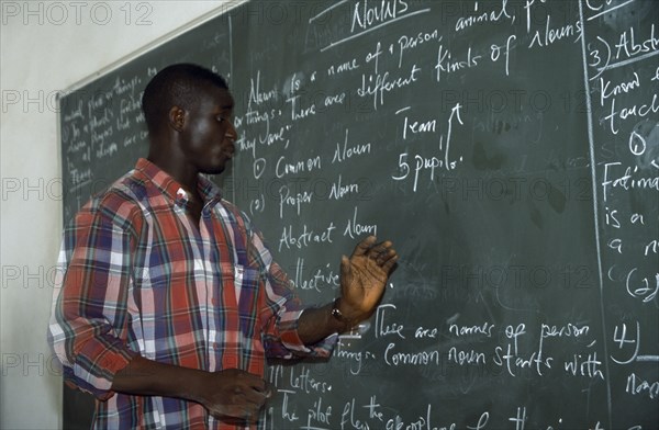 NIGERIA, Kano, English teacher standing beside blackboard giving grammar lesson.