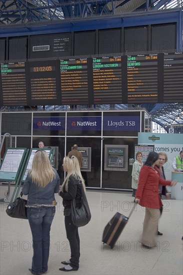 ENGLAND, East Sussex, Brighton, Passengers waiting by noticeboard at the central railway station.