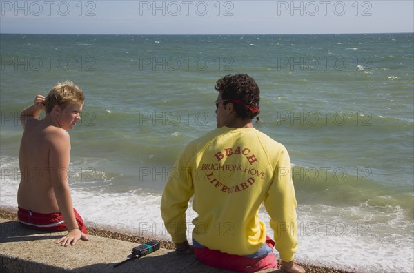 ENGLAND, East Sussex, Brighton, Life guard talking to young boy on the sea wall at Hove.