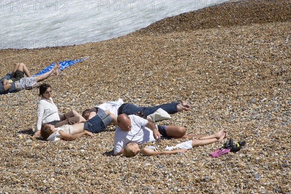 ENGLAND, East Sussex, Brighton, Family on the stoney beach at Hove with father covering son with pebbles.