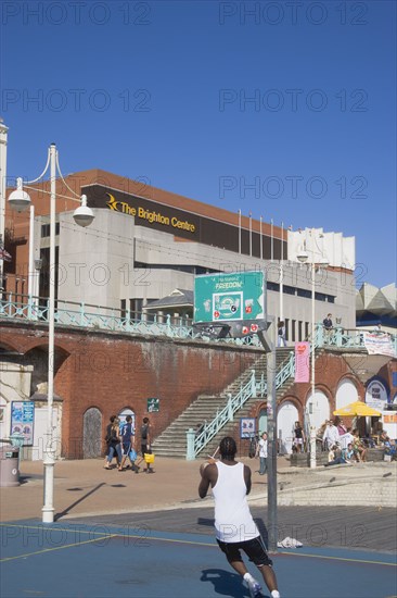 ENGLAND, East Sussex, Brighton, Young man playing basketball on the seafront court with the Brighton Centre behind.