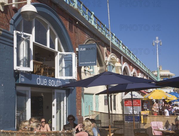 ENGLAND, East Sussex, Brighton, People sat outside the Due South  Restaurant in the arches under the prommenade on the seafront.