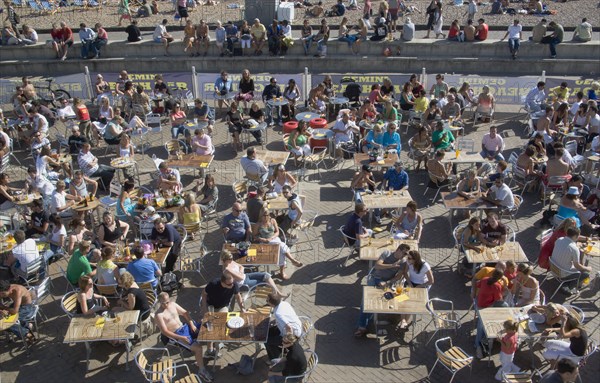 ENGLAND, East Sussex, Brighton, People sat at tables drinking outside the Beach seafront bar.