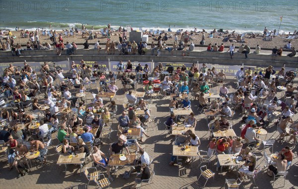 ENGLAND, East Sussex, Brighton, People sat at tables drinking outside the Beach seafront bar.