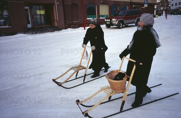 NORWAY, Honningsvag, Female shoppers in snow using single sleds.