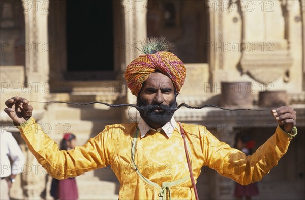 INDIA, Rajasthan, Jaisalmer, Portrait of man displaying the World’s Longest Moustache and wearing beard net and gold coloured jacket.