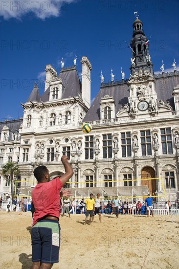 FRANCE, Ile de France, Paris, The Paris Plage urban beach. Young people playing beach volleyball in front of the Hotel de Ville Town Hall with a young man serving