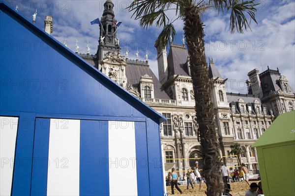 FRANCE, Ile de France, Paris, The Paris Plage urban beach. Young people playing beach volleyball behind beach huts in front of the Hotel de Ville Town Hall