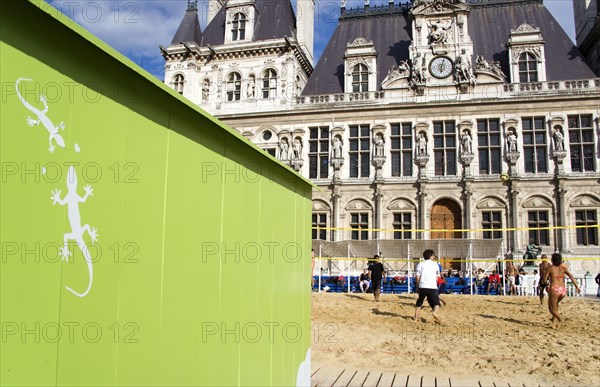 FRANCE, Ile de France, Paris, The Paris Plage urban beach. Young people playing beach volleyball behind a green beach hut with geckos painted on it in front of the Hotel de Ville Town Hall