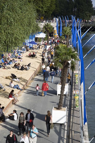 FRANCE, Ile de France, Paris, The Paris Plage urban beach. People strolling between the River Seine and other people lying on sand along the Voie Georges Pompidou usually a busy road now closed to traffic