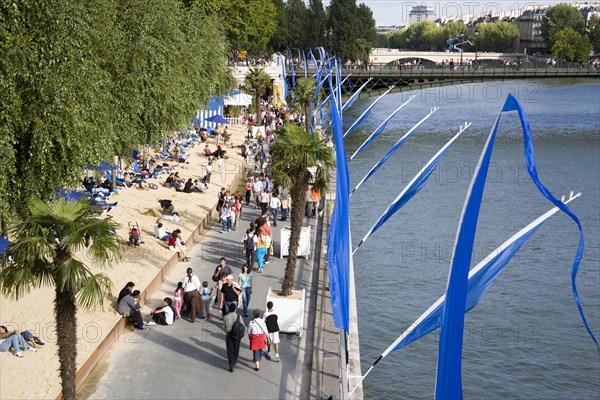 FRANCE, Ile de France, Paris, The Paris Plage urban beach. People strolling between the River Seine and other people lying on sand along the Voie Georges Pompidou usually a busy road now closed to traffic