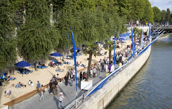 FRANCE, Ile de France, Paris, The Paris Plage urban beach. People strolling between the River Seine and other people lying on sand along the Voie Georges Pompidou usually a busy road now closed to traffic.