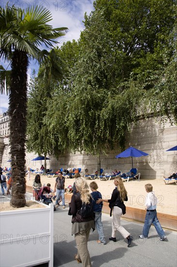 FRANCE, Ile de France, Paris, The Paris Plage urban beach. People strolling between the River Seine and other people lying on sand along the Voie Georges Pompidou usually a busy road now closed to traffic