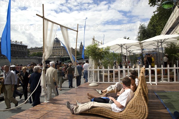 FRANCE, Ile de France, Paris, "The Paris Plage urban beach. People strolling between the River Seine and other people lying on whicker chairs along the Voie Georges Pompidou usually a busy road, now closed to traffic opposite the Ile de la Cite"